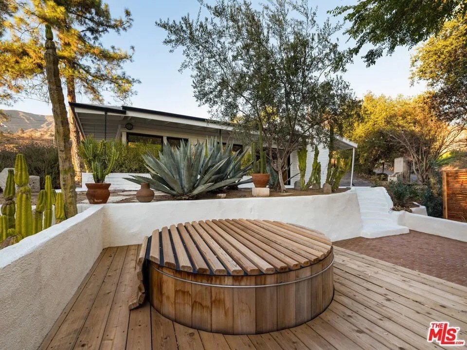 A Jacuzzi sits on a wooden deck right between the two residences, convenient to both.